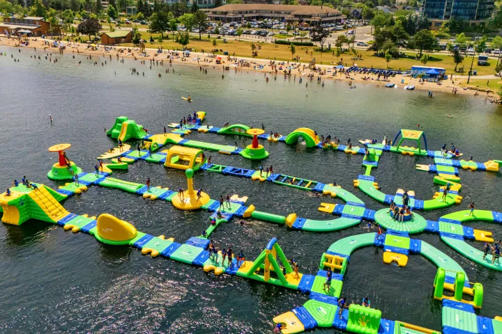 Aerial view of an inflatable water park on a lake with a beach and visitors.