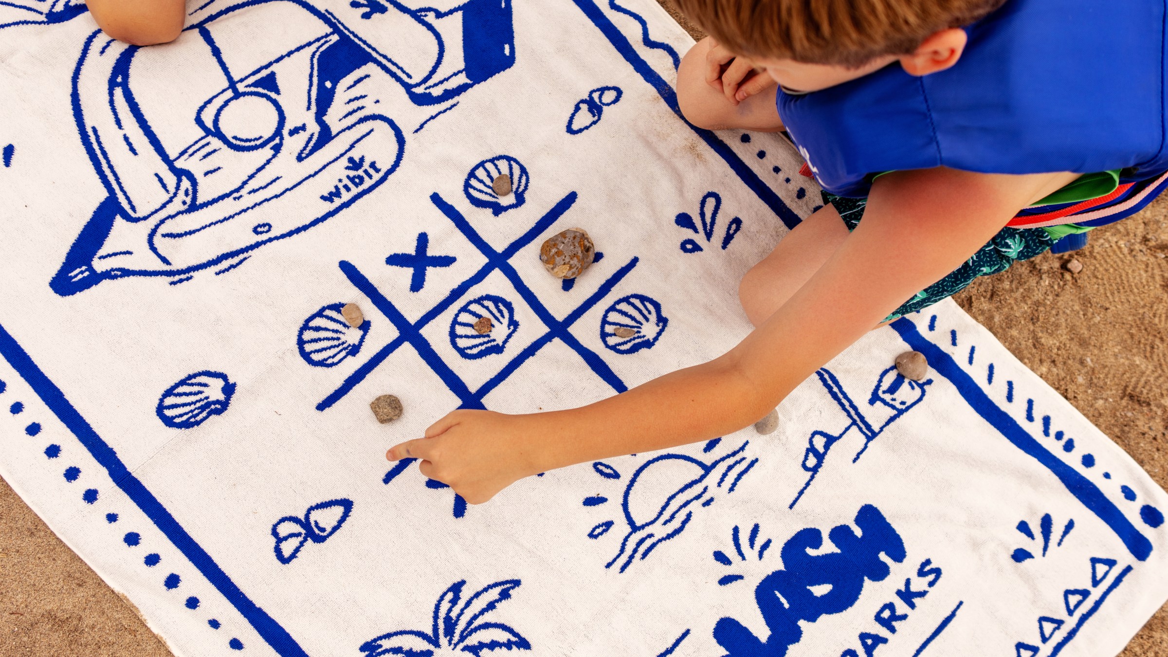 Children playing tic-tac-toe with shells on a beach towel