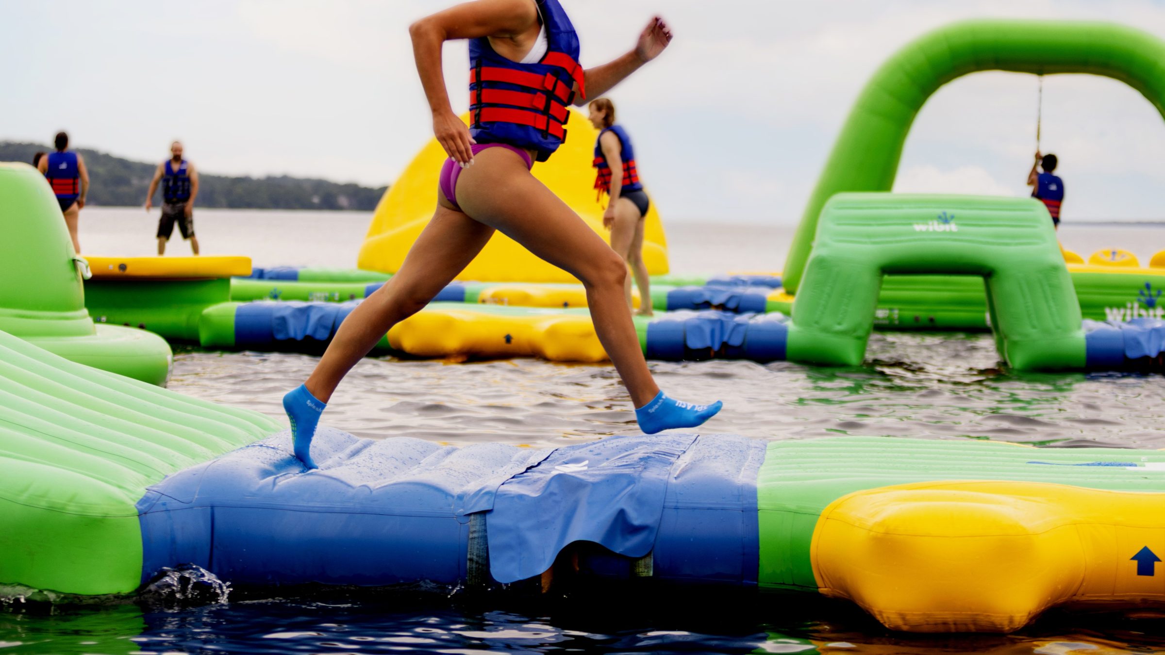 Person running on inflatable water obstacle course in a life jacket.