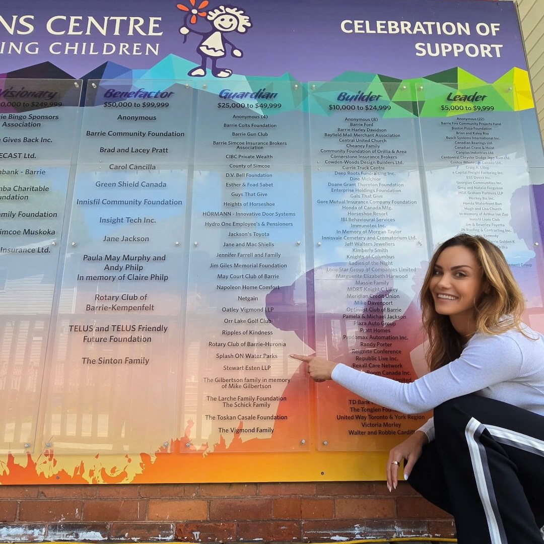 Person pointing at a colorful donor wall at a children's center.