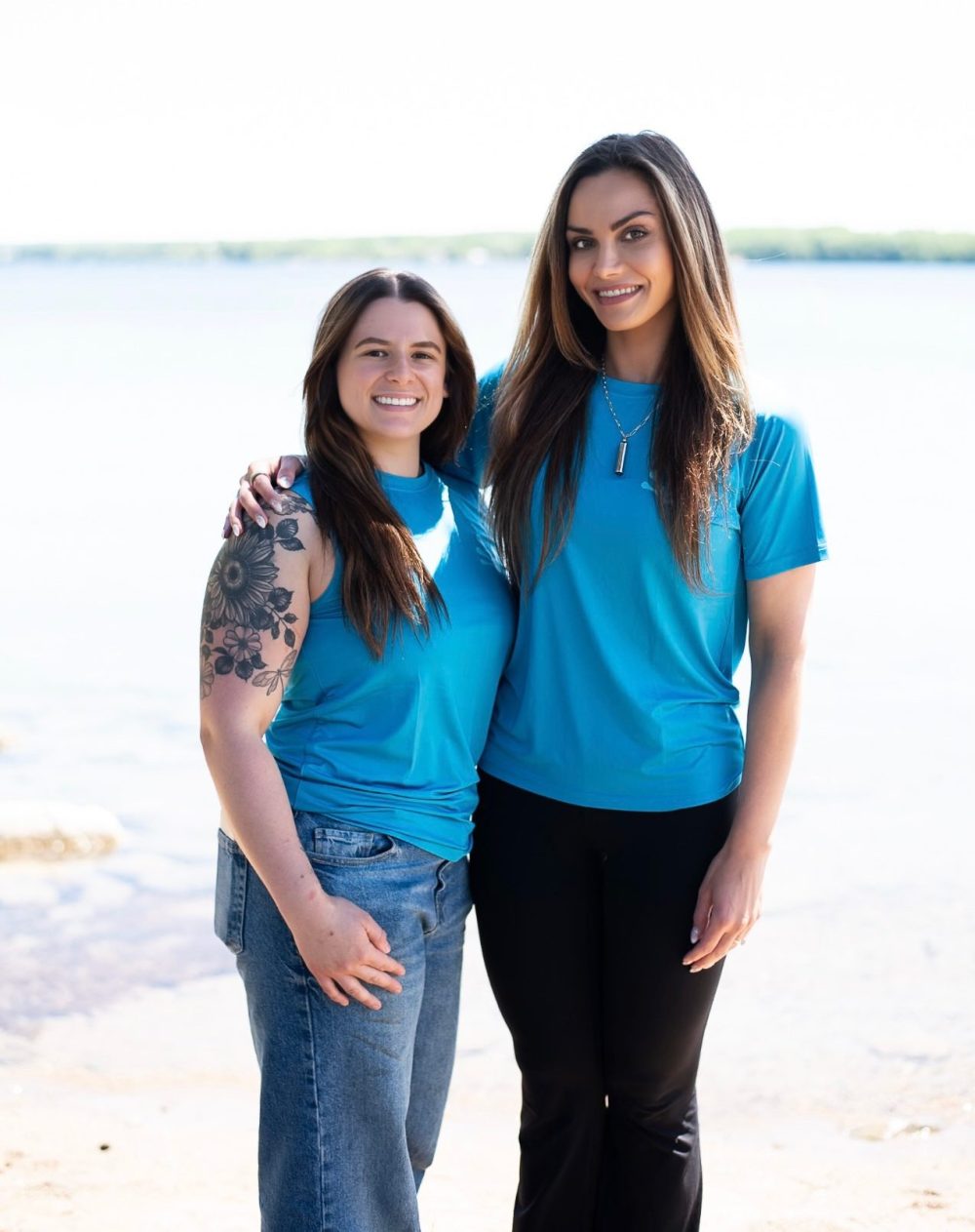 Two people in blue shirts smiling by a lake.